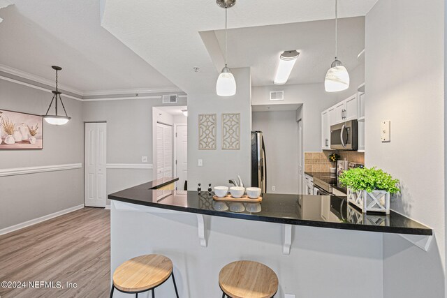 kitchen featuring appliances with stainless steel finishes, a kitchen bar, light wood-type flooring, white cabinets, and pendant lighting