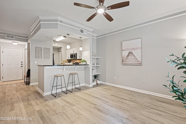 kitchen featuring pendant lighting, ceiling fan, a kitchen bar, light hardwood / wood-style flooring, and ornamental molding