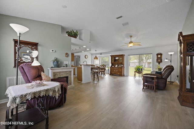 living room with a textured ceiling, a stone fireplace, dark hardwood / wood-style floors, and ceiling fan