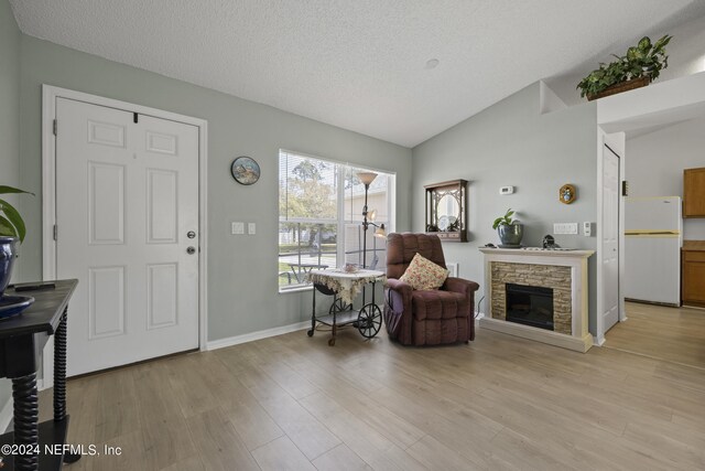 living area featuring lofted ceiling, a textured ceiling, light wood-type flooring, and a fireplace