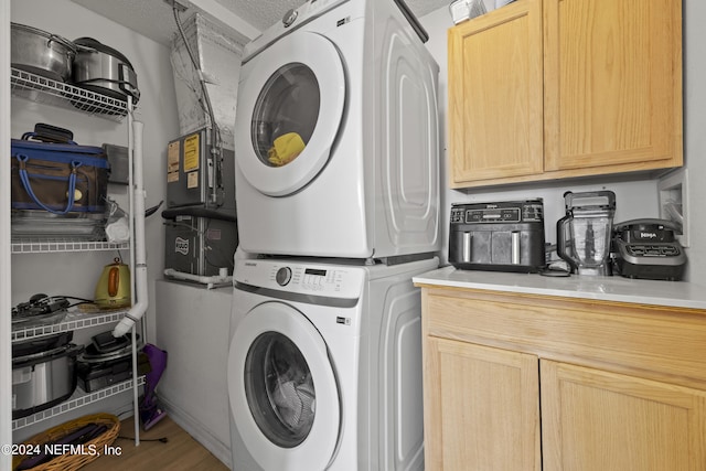 laundry area featuring stacked washer / dryer, cabinets, and light wood-type flooring