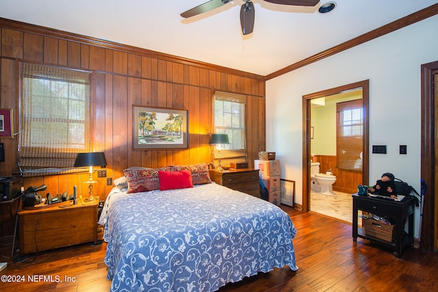 bedroom with dark hardwood / wood-style floors, connected bathroom, wooden walls, ceiling fan, and crown molding