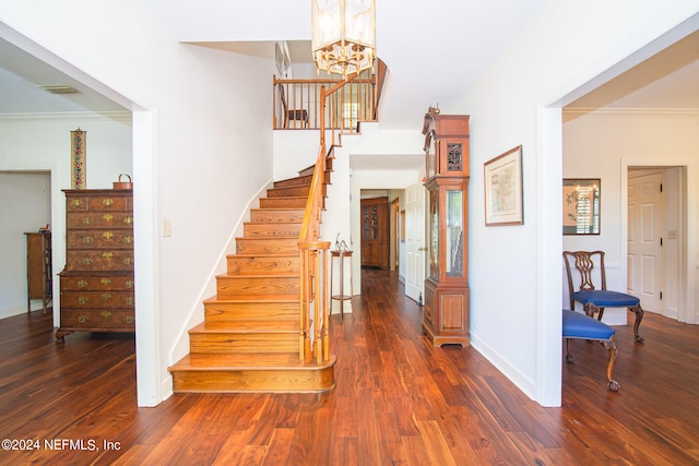 stairs with a chandelier, dark wood-type flooring, and ornamental molding