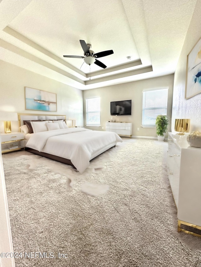 bedroom featuring carpet floors, a tray ceiling, multiple windows, and a textured ceiling