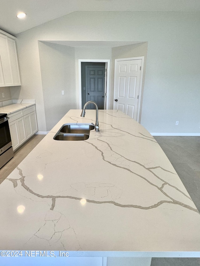 kitchen with light stone counters, a sink, stainless steel range with electric cooktop, vaulted ceiling, and white cabinets