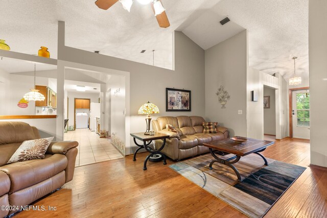 living room with high vaulted ceiling, a textured ceiling, light wood-type flooring, and ceiling fan with notable chandelier