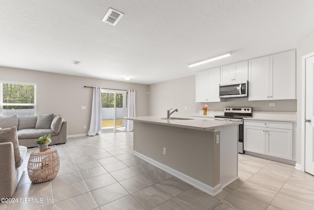 kitchen with an island with sink, light tile floors, appliances with stainless steel finishes, white cabinets, and sink