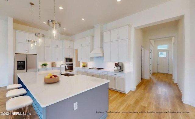 kitchen with pendant lighting, premium range hood, a large island with sink, white cabinetry, and a breakfast bar