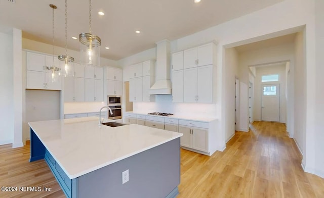 kitchen with white cabinets, decorative light fixtures, custom range hood, and a large island with sink