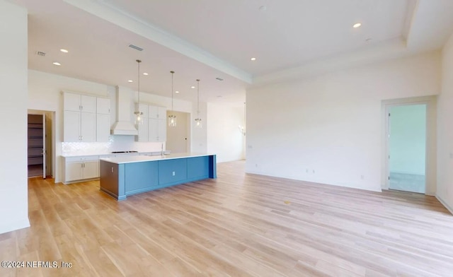 kitchen with hanging light fixtures, a center island with sink, backsplash, white cabinetry, and light hardwood / wood-style floors