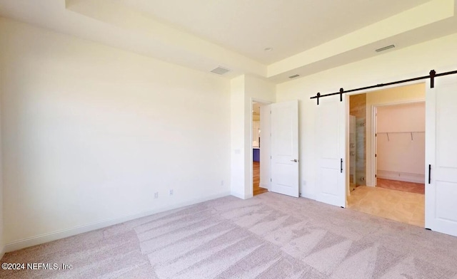 unfurnished bedroom featuring light carpet, a closet, a barn door, and a walk in closet