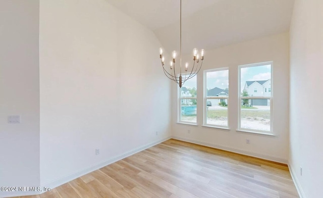 spare room featuring light wood-type flooring, vaulted ceiling, and a notable chandelier