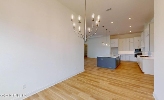 kitchen featuring hanging light fixtures, white cabinetry, sink, and light hardwood / wood-style flooring