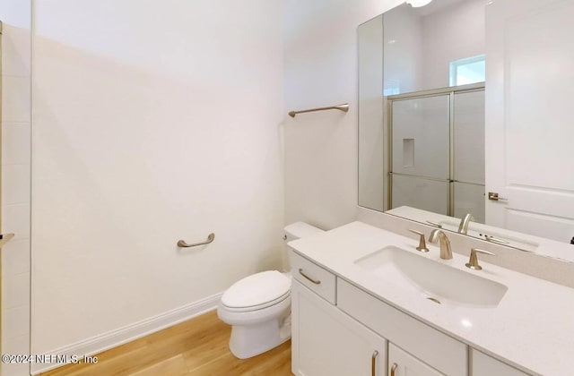 bathroom featuring vanity, hardwood / wood-style floors, a shower with shower door, and toilet