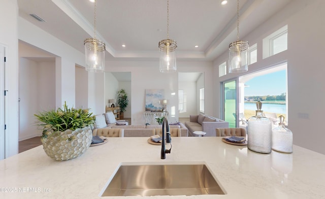 kitchen featuring a raised ceiling, a water view, sink, hanging light fixtures, and light stone counters