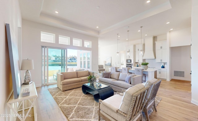 living room with light hardwood / wood-style floors, a raised ceiling, and a water view