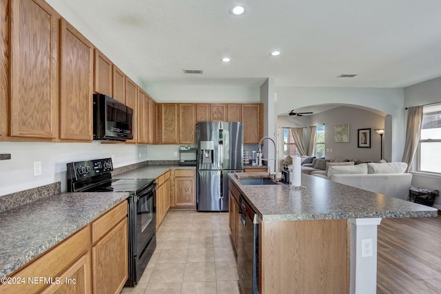 kitchen with a kitchen island with sink, black appliances, light tile floors, sink, and ceiling fan