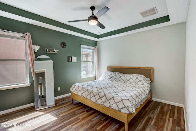 bedroom with wood-type flooring, ceiling fan, and a tray ceiling