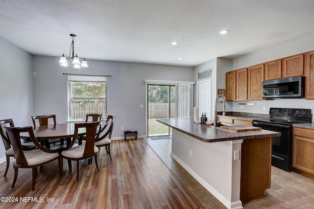 kitchen with decorative light fixtures, tile flooring, a notable chandelier, a center island with sink, and black electric range