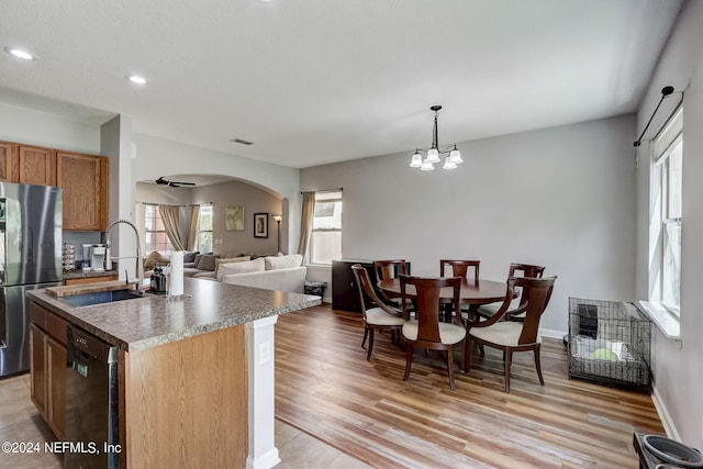 kitchen with black dishwasher, stainless steel refrigerator, light hardwood / wood-style flooring, a center island with sink, and sink