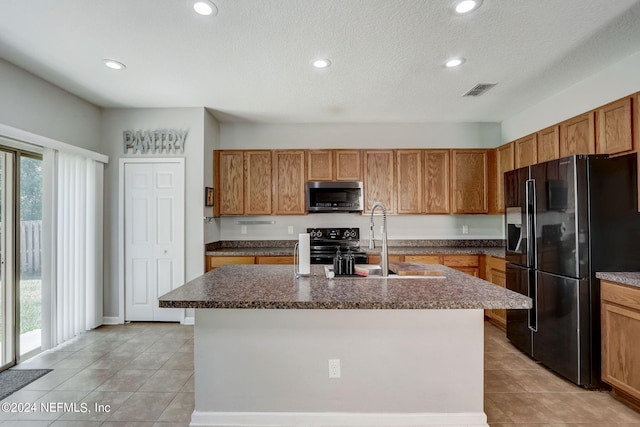 kitchen with an island with sink, a wealth of natural light, light tile floors, and black appliances