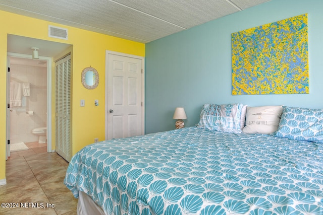 bedroom with light tile floors, a textured ceiling, ensuite bath, and a closet