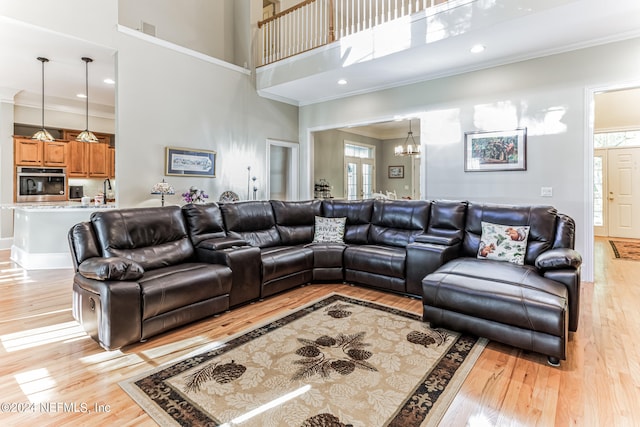 living room with an inviting chandelier, ornamental molding, a high ceiling, and light wood-type flooring