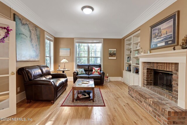 living room with a brick fireplace, ornamental molding, built in shelves, and light hardwood / wood-style flooring