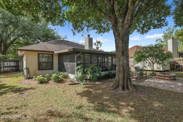 rear view of house featuring a sunroom, an outdoor fire pit, a patio, and a lawn