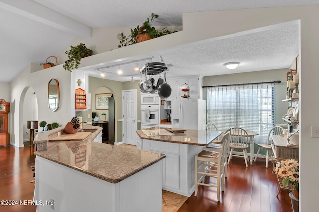 kitchen featuring white appliances, stone counters, a kitchen island, dark hardwood / wood-style flooring, and white cabinetry