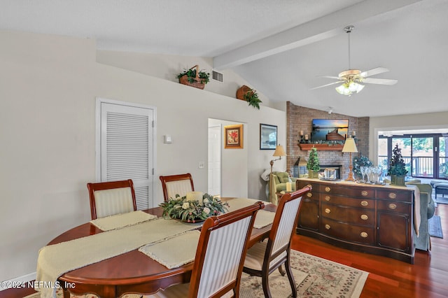 dining space featuring vaulted ceiling with beams, ceiling fan, dark wood-type flooring, and a brick fireplace