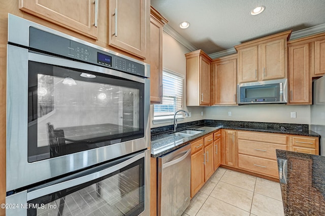 kitchen featuring light tile floors, dark stone counters, appliances with stainless steel finishes, crown molding, and sink