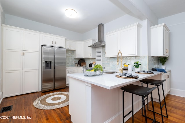 kitchen with white cabinetry, backsplash, wall chimney exhaust hood, and stainless steel refrigerator with ice dispenser