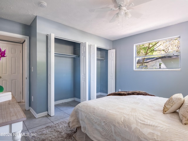 bedroom with multiple closets, ceiling fan, light tile patterned flooring, and a textured ceiling