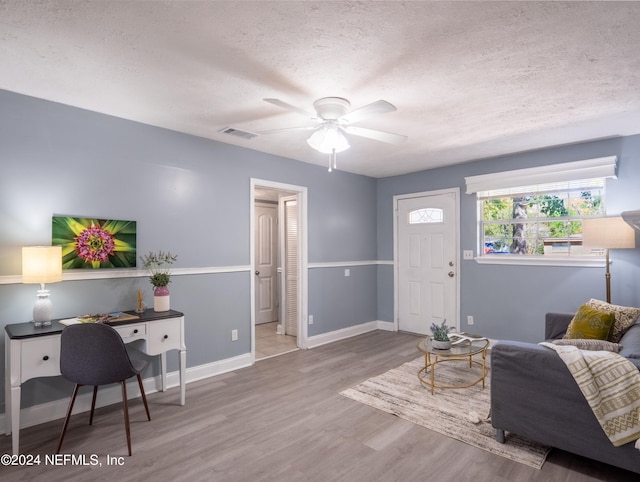 living room with a textured ceiling, ceiling fan, and wood-type flooring