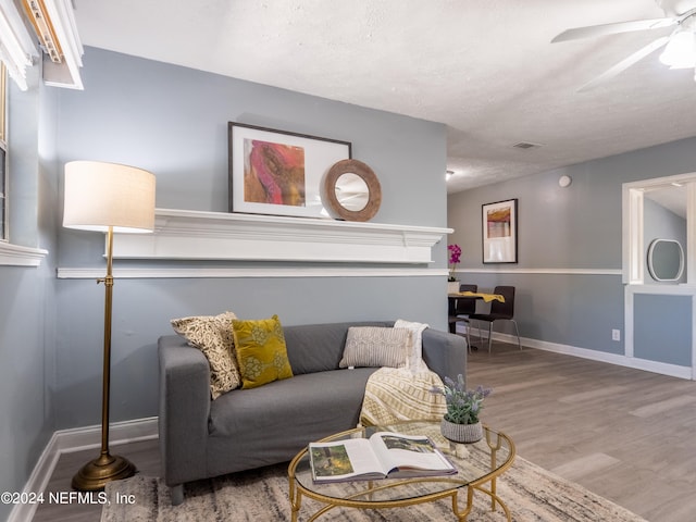 living room with a textured ceiling, ceiling fan, and wood-type flooring