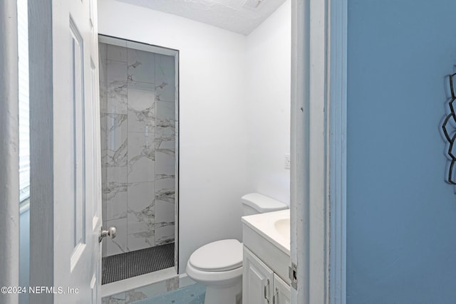 bathroom with toilet, a textured ceiling, a tile shower, and vanity