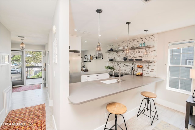 kitchen featuring kitchen peninsula, decorative light fixtures, white cabinets, luxury fridge, and a breakfast bar area