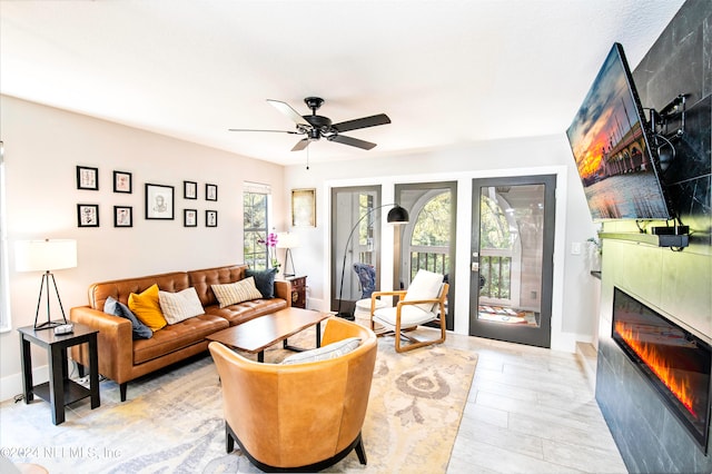 living room featuring a tiled fireplace, ceiling fan, light hardwood / wood-style floors, and a healthy amount of sunlight