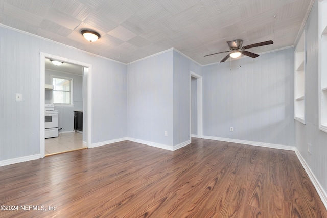 empty room with ornamental molding, wood finished floors, a ceiling fan, and baseboards