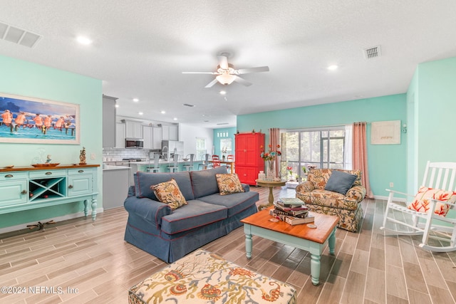 living room featuring ceiling fan, light hardwood / wood-style floors, and a textured ceiling