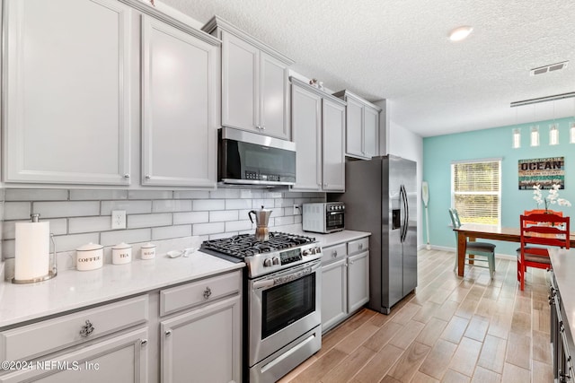 kitchen with decorative backsplash, light wood-type flooring, a textured ceiling, stainless steel appliances, and pendant lighting