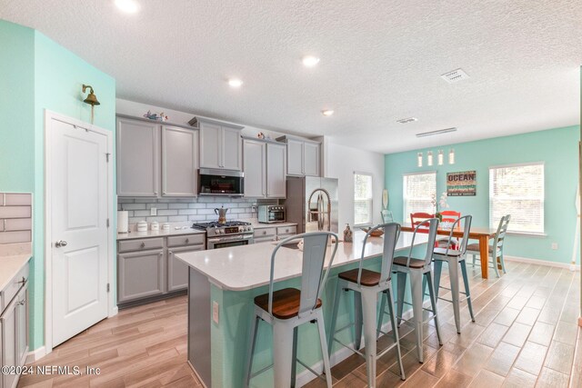 kitchen with a kitchen bar, gray cabinetry, a kitchen island with sink, and stainless steel appliances