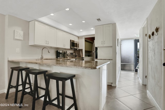 kitchen featuring range, white cabinetry, stone counters, a kitchen breakfast bar, and sink