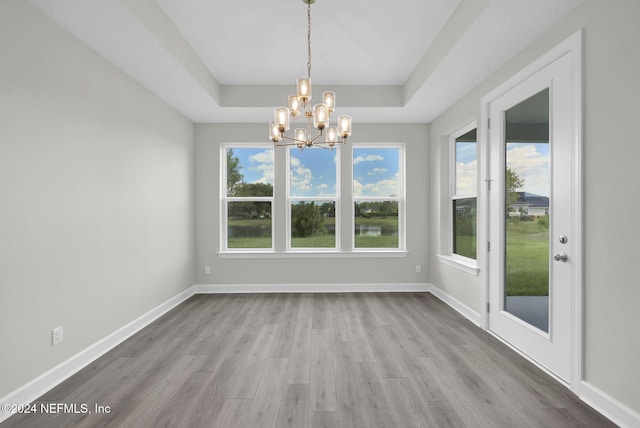 unfurnished dining area with a notable chandelier, a tray ceiling, wood finished floors, and baseboards