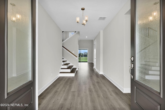 entrance foyer featuring a notable chandelier, visible vents, wood finished floors, baseboards, and stairs