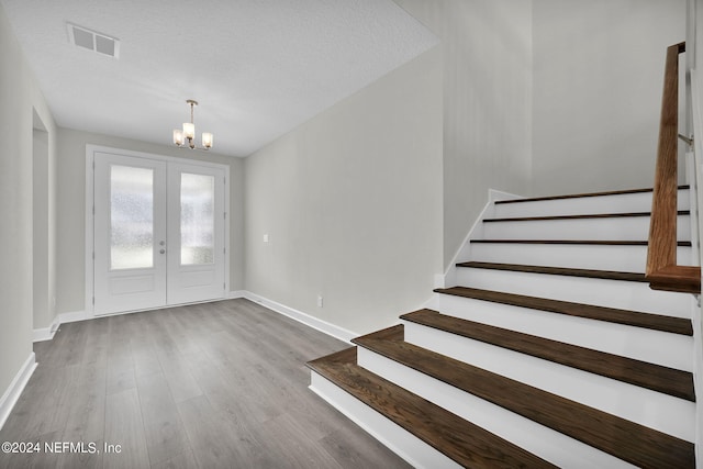 entrance foyer with visible vents, stairway, wood finished floors, an inviting chandelier, and a textured ceiling