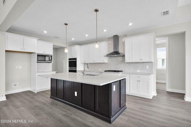 kitchen with stainless steel appliances, tasteful backsplash, sink, light wood-type flooring, and wall chimney range hood