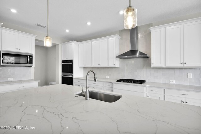 kitchen with wall chimney range hood, tasteful backsplash, appliances with stainless steel finishes, light stone counters, and sink