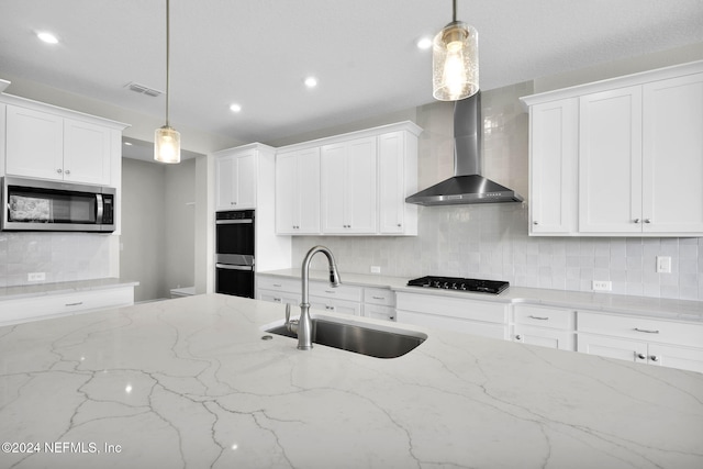 kitchen featuring black cooktop, a sink, visible vents, wall chimney range hood, and stainless steel microwave